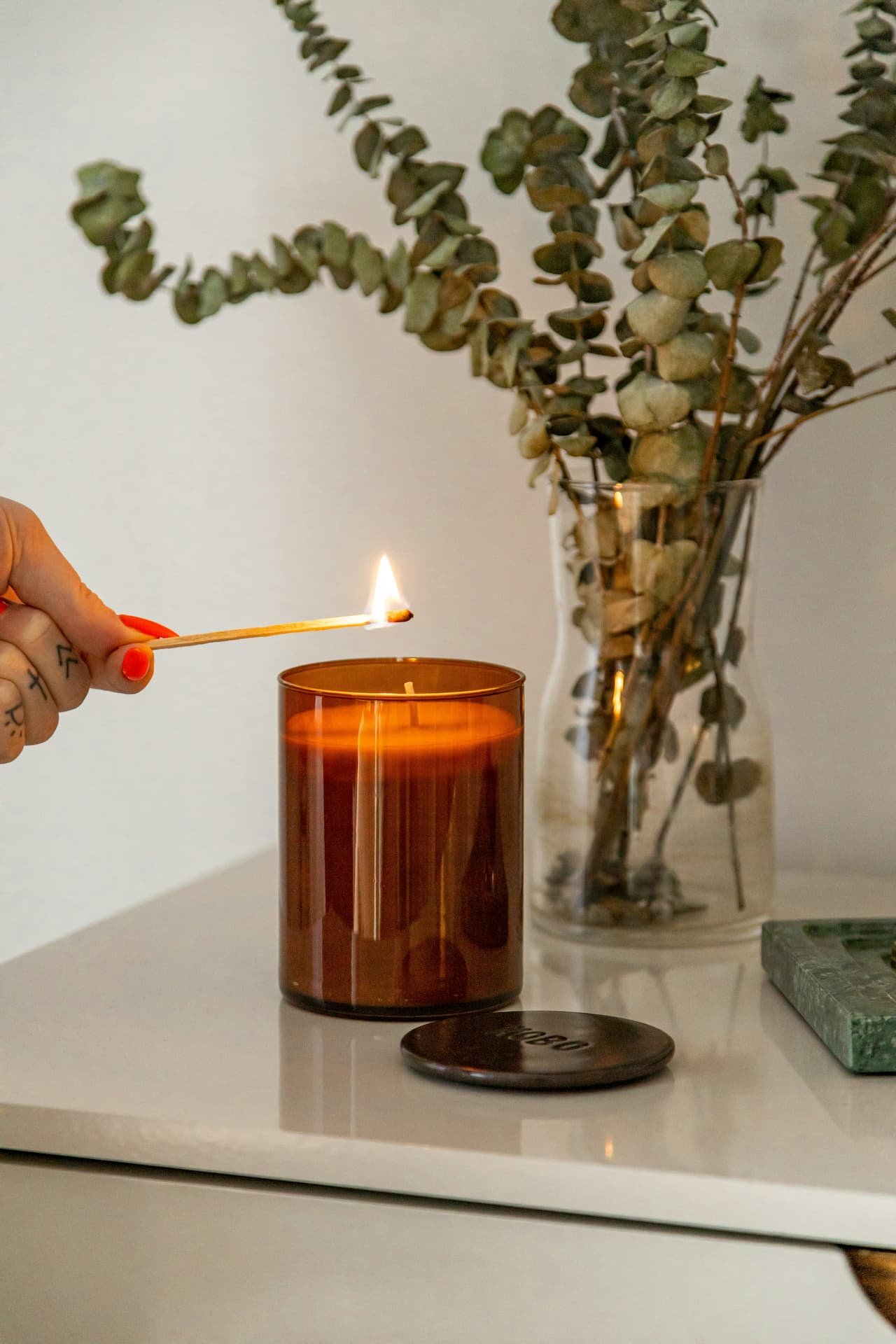 Vela ámbar encendiéndose con fósforo junto a ramas de eucalipto